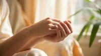 Woman applying hand cream or moisturizer for skincare routine in natural sunlight. Self-care wellness beauty treatment at home spa relaxation.