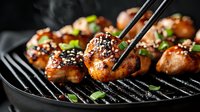 Grilled Asian-style chicken wings with sesame seeds and green onions on black grill pan, glazed in sweet and savory sauce, close up view in dark moody lighting.
