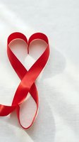 Red satin ribbon twisted into heart shape on white fabric background for romantic occasions, weddings, Valentine's Day celebrations and love concepts.