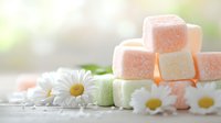 Pastel colored marshmallows stacked with fresh white daisies on light background, soft focus composition with delicate morning light and dreamy atmosphere.