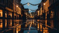 Festive city street with warm golden lights and decorations reflected on wet pavement during evening hours creating magical holiday atmosphere for celebrations.