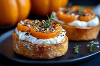 Mini pastry tarts filled with whipped cream, topped with fresh apricot slices, thyme sprigs and black sesame seeds on dark plate, close up view.