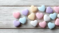 Colorful pastel heart-shaped candies scattered on white wooden background. Sweet romantic treats in soft pink, blue, purple and cream colors for Valentine's Day.