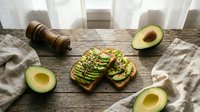 Avocado toast on rustic wooden board with fresh halved avocados, pepper mill and linen napkin. Healthy breakfast or brunch meal concept for social media content.