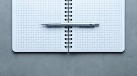 Open spiral notebook with grid paper and silver pen on gray surface for planning, note-taking, sketching, and office work projects.