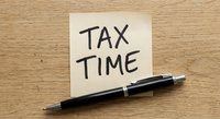 Sticky note with tax time reminder and black pen on wooden desk surface for financial planning and accounting preparation during filing season.