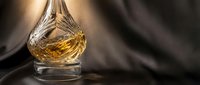 Elegant crystal whiskey decanter with amber liquid on dark fabric background, luxury barware for sophisticated drinking experience and home bar decoration.