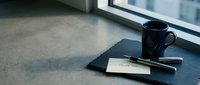 Thank you card with pen and dark blue mug on slate tray near window, elegant desk setup for gratitude and professional correspondence.