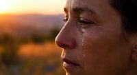 Emotional middle-aged woman with tears streaming down face during golden hour sunset, profile view showing deep contemplation and sadness.