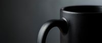 Black ceramic coffee mug close-up with handle detail on dark background for kitchen and beverage concepts in moody lighting atmosphere.