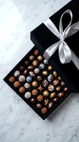 Luxury chocolate assortment in black gift box with white ribbon bow on marble surface, overhead view for confectionery, gifting, and food styling projects.