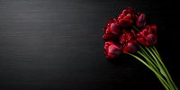 Fresh red tulips bouquet on dark black wooden background, dramatic lighting creates elegant mood for romantic occasions and luxury floral design concepts.