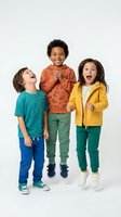 Three diverse children laughing and playing together in colorful casual clothing on white background, expressing joy and friendship for kids fashion.