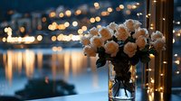 Elegant white roses in glass vase against evening cityscape with bokeh lights reflecting on water surface, creating romantic ambiance for special occasions.