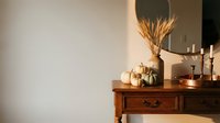 Cozy autumn home interior with pumpkins, wheat bundle, candles on wooden dresser creating warm seasonal atmosphere for fall decorating and lifestyle.