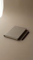 Closed notebook with gray cover and two black pens on neutral beige surface with soft natural lighting, suitable for business, education, and stationery design projects.