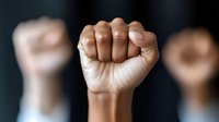 Raised fists in solidarity gesture showing unity and empowerment in protest or activism movement with blurred background of supporters.