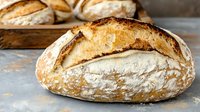Freshly baked artisan sourdough bread loaves with golden crust and flour dusting on rustic wooden surface for bakery and food photography.