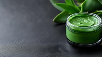 Green aloe vera gel in glass jar with fresh plant leaves on dark slate background for natural skincare and cosmetic products.