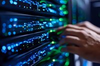 Network administrator hands working on server rack with glowing blue and green LED indicators in modern datacenter, focused on maintenance and connectivity.
