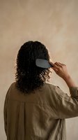 Woman with curly hair combing wet locks with wide-tooth comb in natural light for haircare routine and styling concept.