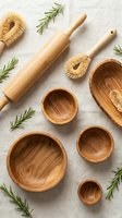 Natural wooden kitchen utensils and bowls with fresh rosemary herbs arranged on linen fabric for cooking and baking preparation.