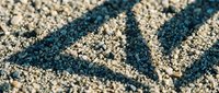 Geometric triangle pattern drawn in sand with finger creating textured lines and shadows for creative design projects and artistic backgrounds.