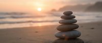 Zen stone stack on beach at sunset with golden sky and ocean waves creating peaceful meditation and balance concept for wellness and mindfulness practices.