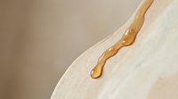 Honey dripping from wooden dipper onto white ceramic plate, golden liquid flow, cooking and baking ingredient for culinary design projects.