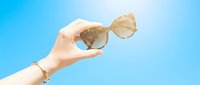 Close-up of a woman's hand holding stylish sunglasses against a clear blue sky, perfect for summer fashion, travel, and lifestyle marketing campaigns.