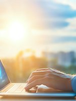 Female hands typing on laptop keyboard at sunset, with golden sunlight creating atmospheric backlight and soft bokeh effect, ideal for remote work concepts.