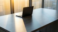 Laptop on modern minimalist desk with natural light from windows, suitable for business, technology, and workspace concepts.