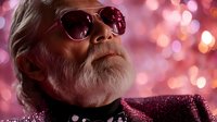 Senior Caucasian man with white beard wearing sunglasses and glitter jacket against pink bokeh background, creating stylish and confident mature fashion portrait.