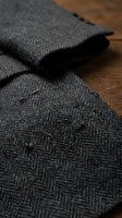 Gray herringbone wool fabric folded on wooden surface showing detailed weave pattern and textile texture for fashion and tailoring projects.