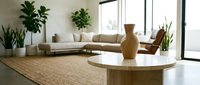 Modern minimalist living room interior with beige sectional sofa, round coffee table, wooden vase, and large windows creating bright natural lighting.