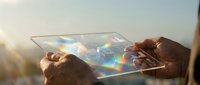 Young adult male with medium brown skin tone holding transparent digital tablet displaying colorful holographic interface with data visualization, outdoor setting with golden sunlight, technology and innovation concept for business applications.