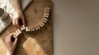Woman arranging wooden letter blocks spelling GRATEFUL on rustic table surface, expressing gratitude and mindfulness in cozy home setting.