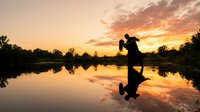 Romantic couple silhouette dancing by tranquil lake at golden sunset with perfect water reflection creating dreamy atmosphere for wedding and love concepts.