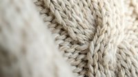 Close-up macro shot of beige knitted wool fabric showing detailed cable stitch pattern and texture for cozy winter fashion and textile design projects.