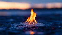 Orange flame burning on dark rocky surface against blurred blue twilight background, creating atmospheric mood with selective focus on dancing fire.