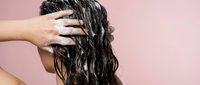 Woman applying hair mask treatment to wet curly hair for deep conditioning and nourishment against pink background.