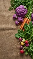 Fresh organic vegetables including purple cauliflower, carrots, radishes and leafy greens arranged on rustic burlap background for healthy cooking and nutrition.