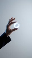 Hand in dark suit sleeve holding glowing circular light symbol against light gray background, futuristic technology concept.