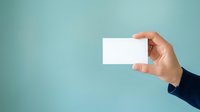 Hand holding blank white business card against turquoise background, ready for branding, corporate identity, and marketing design projects.