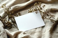 Blank white card mockup with dried flowers on neutral beige linen fabric background. Romantic minimal flat lay composition for wedding stationery or branding.