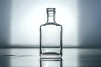 Empty glass bottle with square shape and short neck on reflective surface against gradient background, dramatic studio lighting creates elegant shadows.