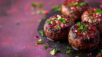 Glazed chocolate donuts with berry topping and fresh mint leaves on dark purple background. Sweet dessert food photography for bakery menu design.