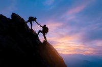 Silhouette of climbers helping each other on mountain peak against dramatic purple and orange sunset sky, symbolizing teamwork and achievement in nature.
