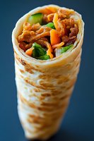 Fresh bacon wrap with crispy strips, colorful vegetables and lettuce rolled in soft flatbread tortilla against dark blue background, close up food photography.