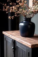 Moody still life with navy blue ceramic vase holding dried pink blossoms on rustic wooden cabinet top, dark interior design composition with dramatic lighting.